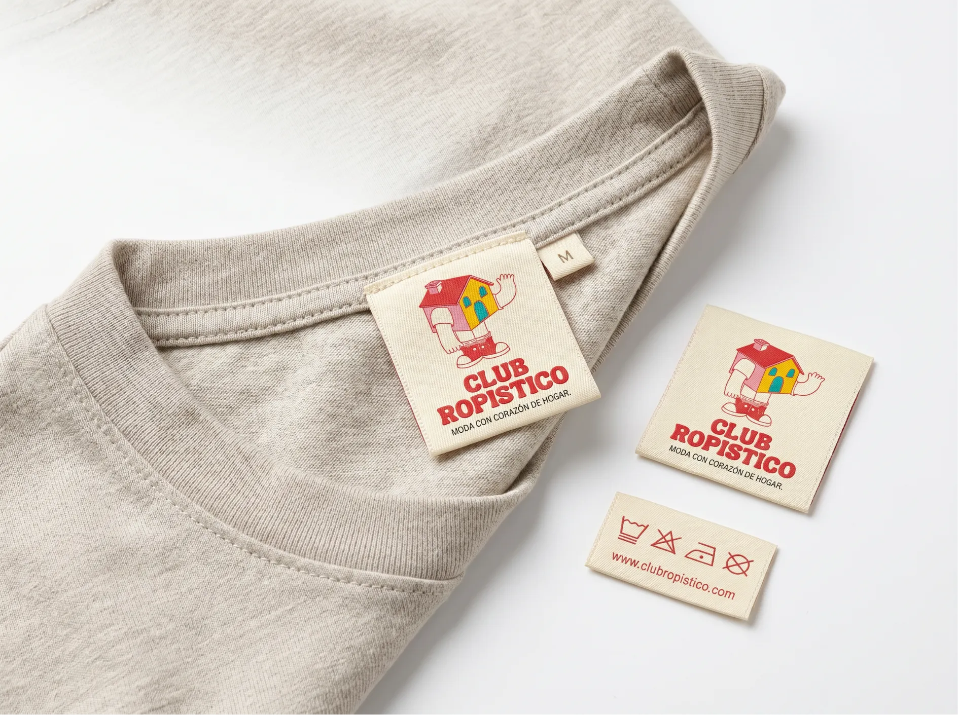 A cream woven house mascot label sewn into a cotton tee, with matching brand and care labels.
